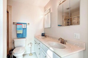 Ein Badezimmer mit Toilette, zwei Waschbecken, einem Spiegel und einem Handtuchhalter.