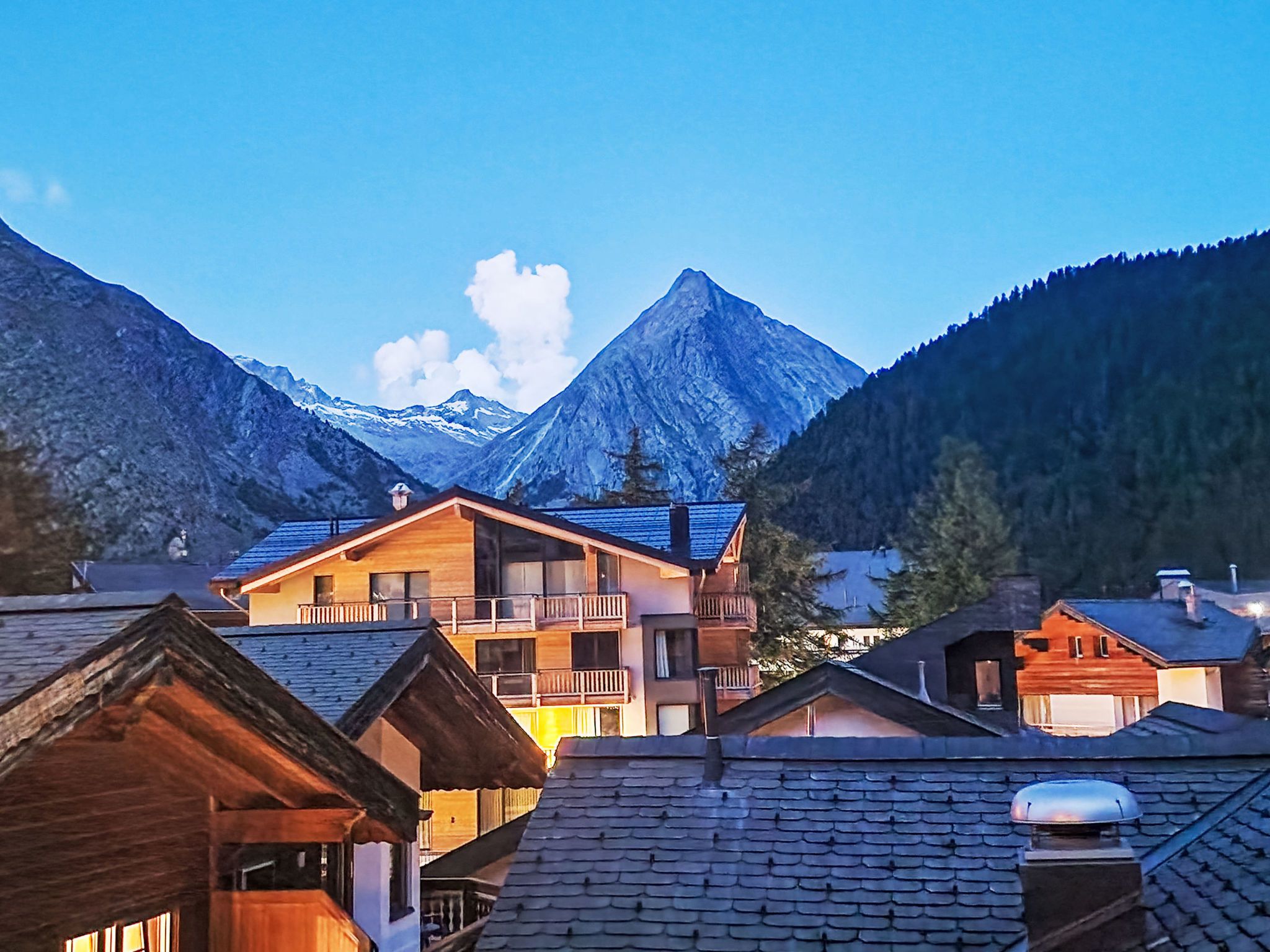 Un village de montagne aux maisons en bois, avec un sommet imposant en arrière-plan et un ciel dégagé.