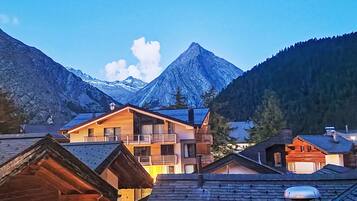 Un village de montagne aux maisons en bois, avec un sommet imposant en arrière-plan et un ciel dégagé.