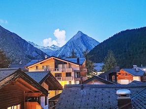 Un village de montagne aux maisons en bois, avec un sommet imposant en arrière-plan et un ciel dégagé.