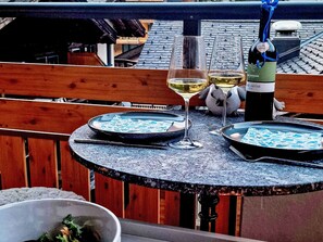 Ein runder Tisch mit zwei Tellern Essen, zwei Weingläsern und einer Weinflasche auf einem Balkon.