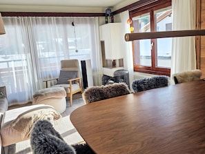 A cozy room with a wooden table, two chairs, a sofa, and a window with curtains. - Wohnung Auri by Interhome (Saas-Fee)
