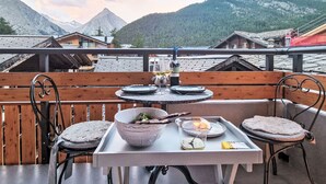 En terrasse med et spisebord med dække, med udsigt over et bjergrigt landskab.