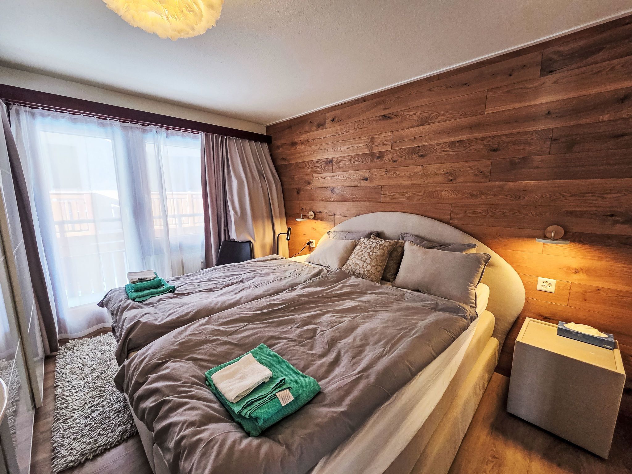 Une chambre à coucher moderne avec un mur en bois, un grand lit avec une literie grise, une table de chevet et une commode.