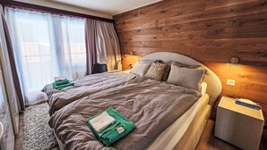 Et moderne soveværelse med en trævæg, en stor seng med gråt sengetøj, et natbord og et sengebord.
