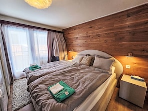 Une chambre à coucher moderne avec un mur en bois, un grand lit avec une literie grise, une table de chevet et une commode.