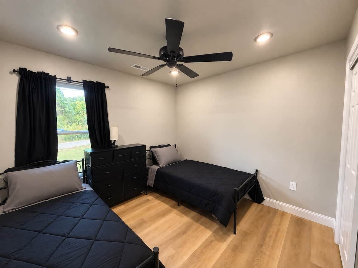 Une chambre avec deux lits, un ventilateur de plafond, une commode et une fenêtre avec des rideaux.