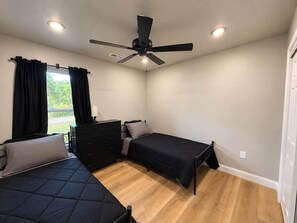 Une chambre avec deux lits, un ventilateur de plafond, une commode et une fenêtre avec des rideaux.