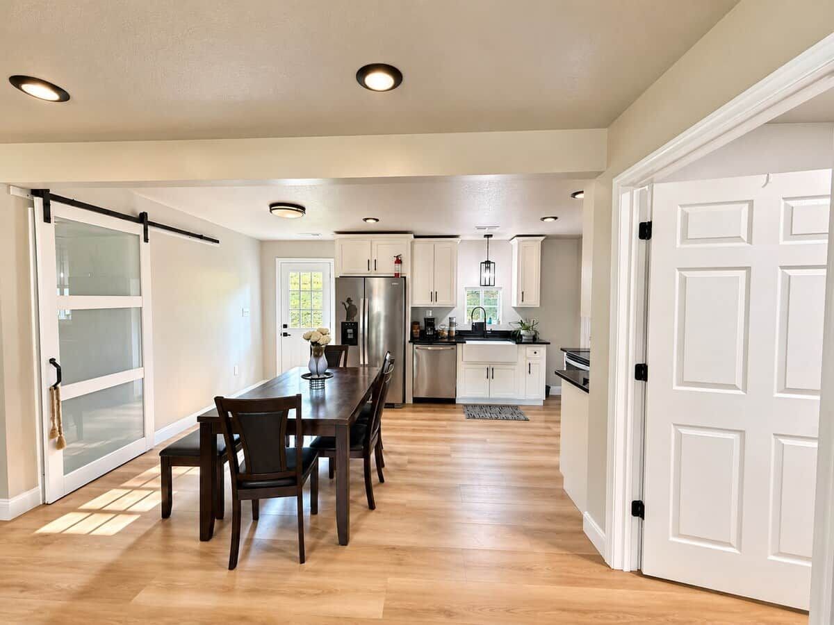 A modern kitchen with a dining area, white cabinetry, and a large window.