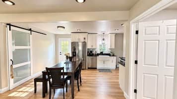 A modern kitchen with a dining area, white cabinetry, and a large window.