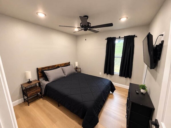 A bedroom with a bed, a nightstand, a TV, and a ceiling fan.