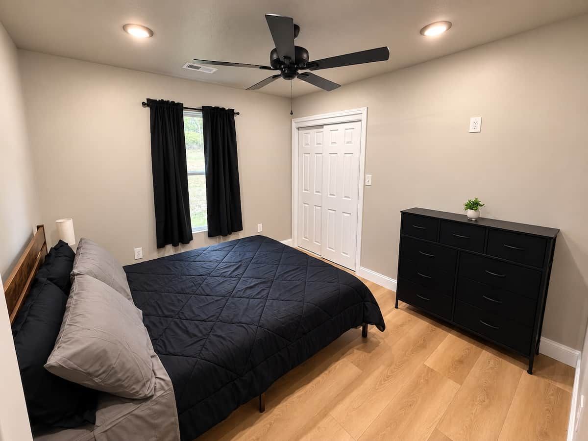 Un dormitorio con cama, cómoda, ventilador de techo y puerta.