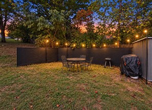 A backyard with a covered patio table and chairs, surrounded by a black fence, and string lights.