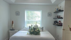 Quarto com cama, ventoinha no teto, janela com persianas, mesa de cabeceira, prateleira com troféus e porta.