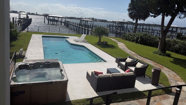 Piscina com hidromassagem, área de estar ao ar livre e vista para um corpo d'água com cais.