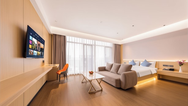 Ein modernes Hotelzimmer mit Flachbildfernseher, einer Couch, einem Esstisch und einem Bett.