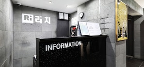 Una zona de recepción con un mostrador negro identificado con 'INFORMATION' y un reloj en la pared.