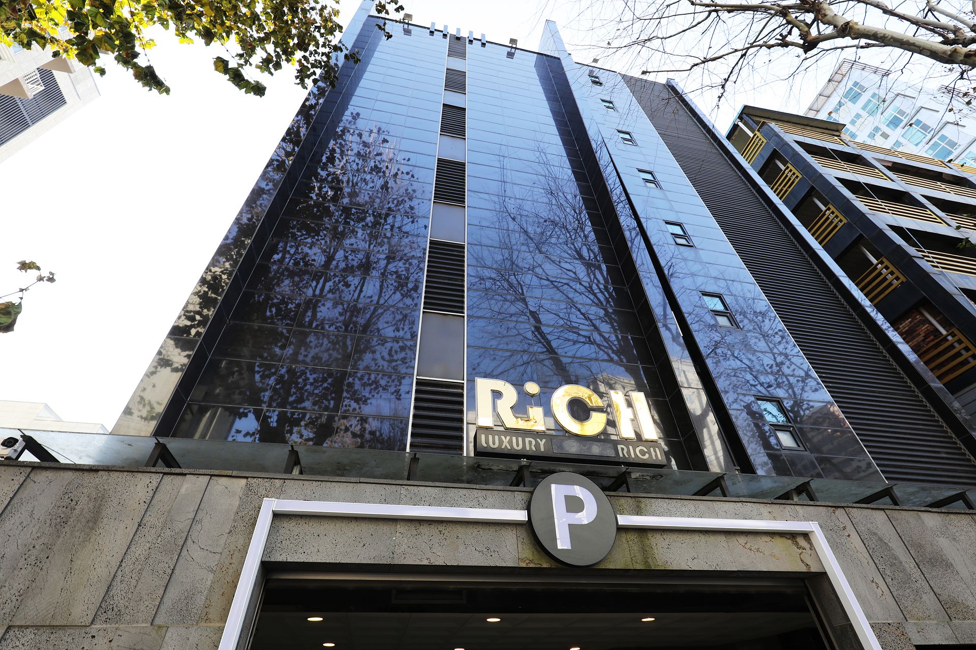 Un edificio alto con un gran fachada de vidrio reflectante, un cartel de hotel de lujo y una señal de estacionamiento.