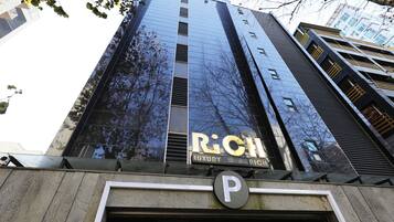 Un edificio alto con un gran fachada de vidrio reflectante, un cartel de hotel de lujo y una señal de estacionamiento.