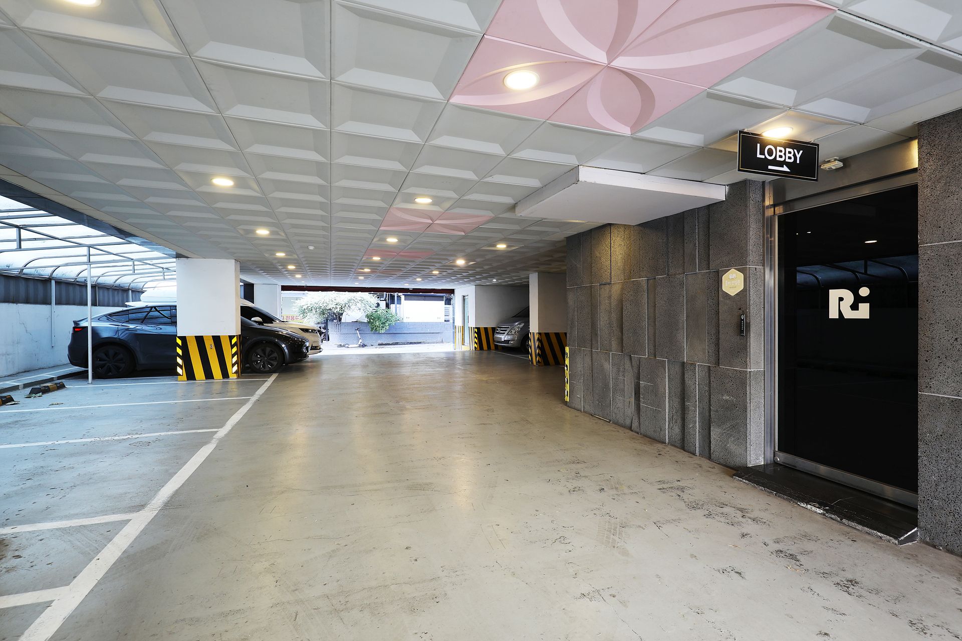 A parking garage with a 'Lobby' sign, a car parked by the wall, and a building entrance with a 'R' logo.