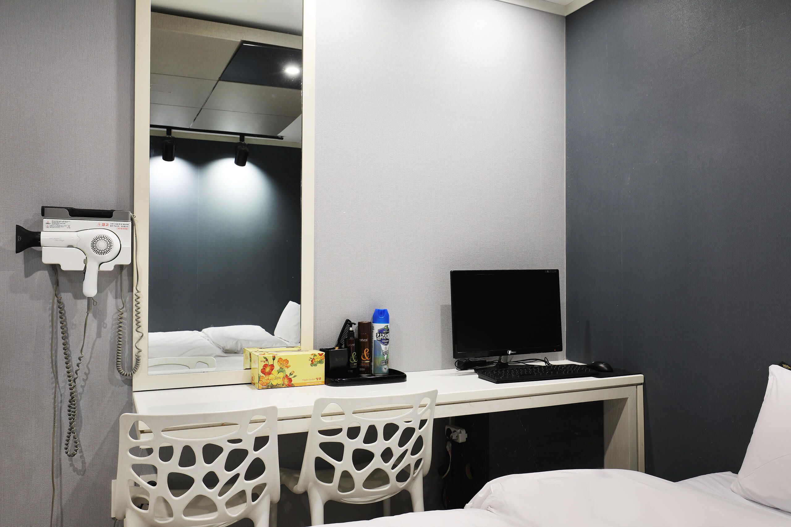 A hotel room with a bed, a desk with a computer, a mirror, and a hairdryer.
