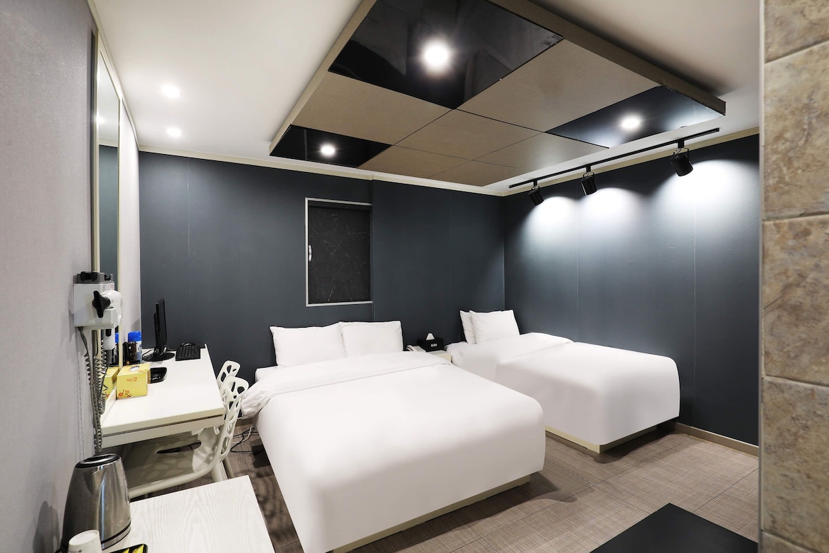 Habitación de hotel con dos camas, un escritorio con computadora, un secador de pelo y un espejo.