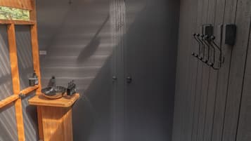 A shower enclosure with a wooden bench and a sink, a towel rack, and a showerhead.