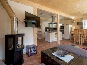 Ein modernes Interieur mit Holzboden und -verkleidung, einem schwarzen Kaminofen, einem Flachbildfernseher, einer Küchenzeile und einem Essbereich mit Holzkästen.