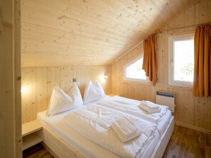 Ein Zimmer mit Holzboden, einem Bett mit weißer Bettwäsche, einem Fenster mit Vorhängen und einem Wandheizkörper.