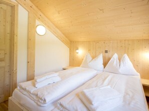 Ein Zimmer mit Holzwandverkleidung, einem Bett, Kissen und einer wandmontierten Leuchte.