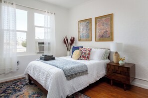 Un dormitorio con cama, mesita de noche, lámpara y una obra de arte en la pared.