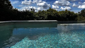 A clear swimming pool with a stone edge, surrounded by dense greenery. - Hilltop Getaway (Ocean View)