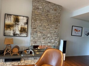 A living room with a stone fireplace, a sofa, a lamp, and framed artwork on the wall. - Hilltop Getaway (Ocean View)