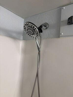 A showerhead with a flexible hose, mounted on a wall with a textured surface. - Driftwood Studio | Steps to South Myrtle Beach ,Bright, Cozy & Self Check-In (Myrtle Beach)