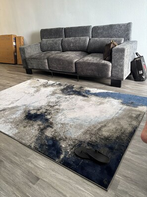 A grey sofa, a blue and white patterned rug, and a black bag on a wooden floor. - Driftwood Studio | Steps to South Myrtle Beach ,Bright, Cozy & Self Check-In (Myrtle Beach)