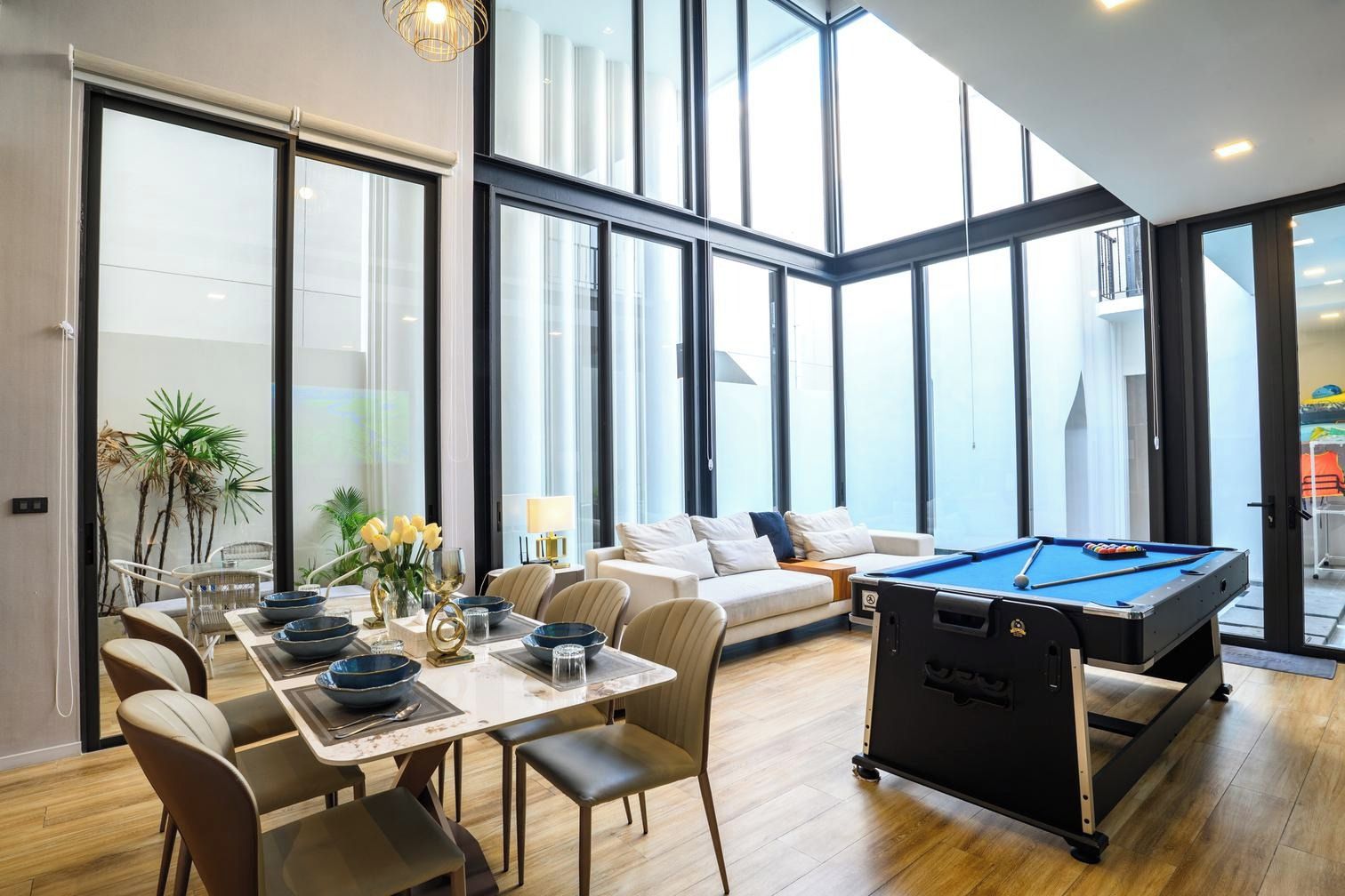 A modern living room with a pool table, a dining area with a table set for two, and a sofa.