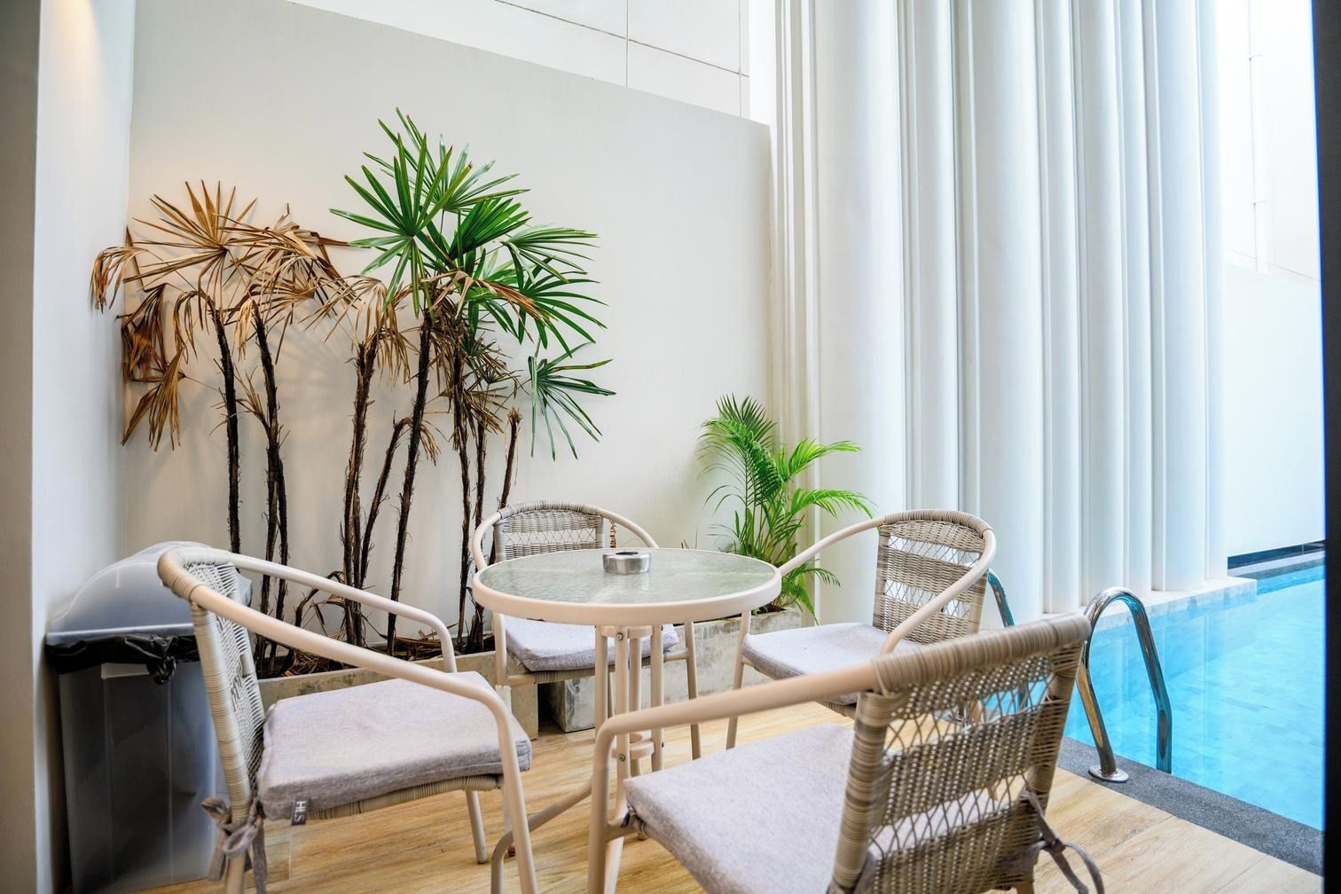 A room with a pool, wicker chairs, a round table, and potted plants.