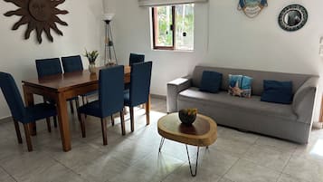 A dining area with a wooden table and blue chairs, a grey sofa with blue cushions, and a decorative sun on the wall.