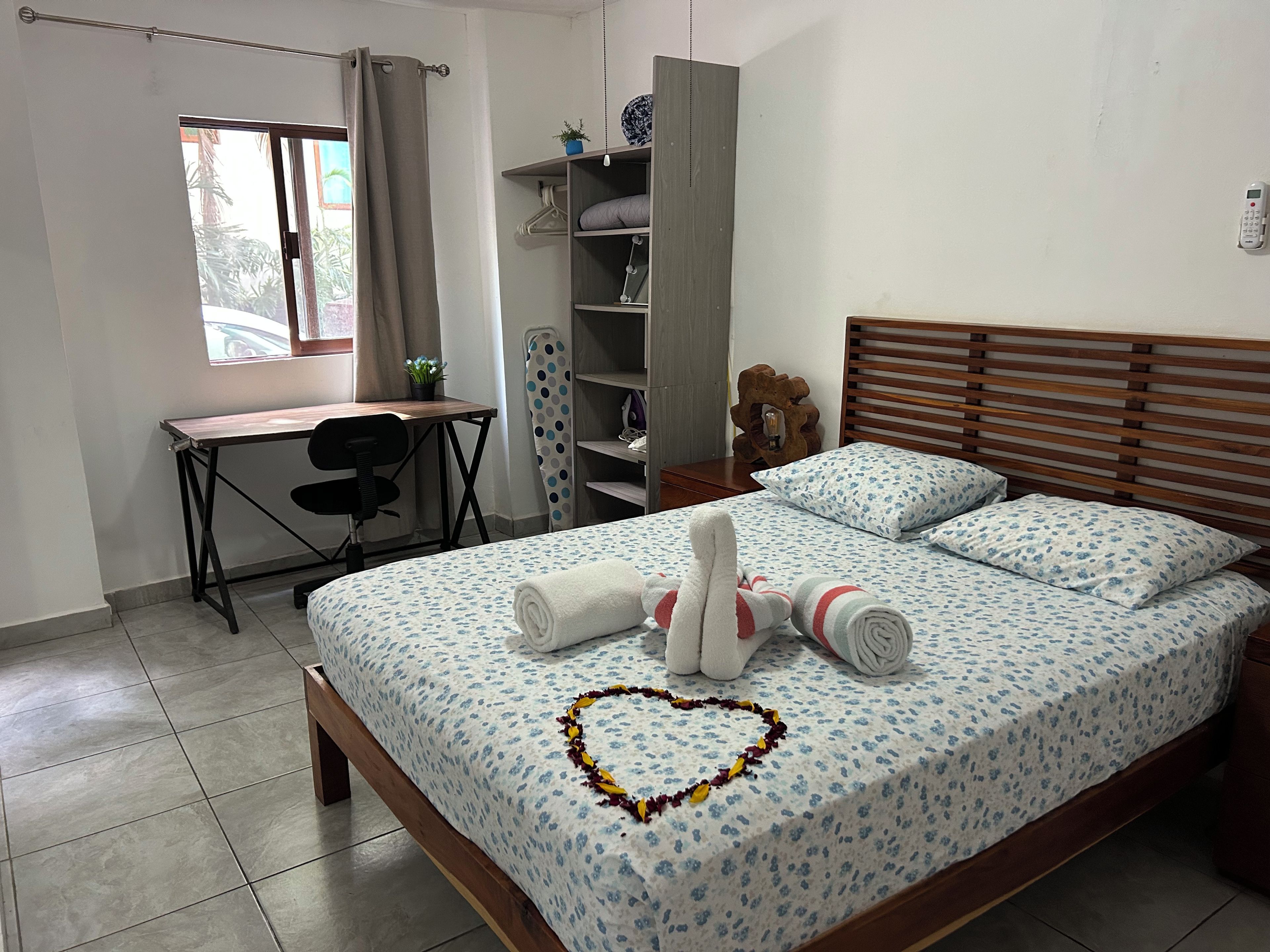 A bedroom with a bed, a desk, a chair, a wardrobe, and a bedside table.