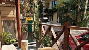 An outdoor seating area with wooden tables and stools, surrounded by potted plants and a wooden fence. - Blue Angel 4, just a few steps from 5th Avenue (Playa del Carmen)