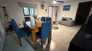A dining area with a wooden table and blue chairs, a grey sofa, a ceiling fan, and a TV. - Blue Angel 4, just a few steps from 5th Avenue (Playa del Carmen)