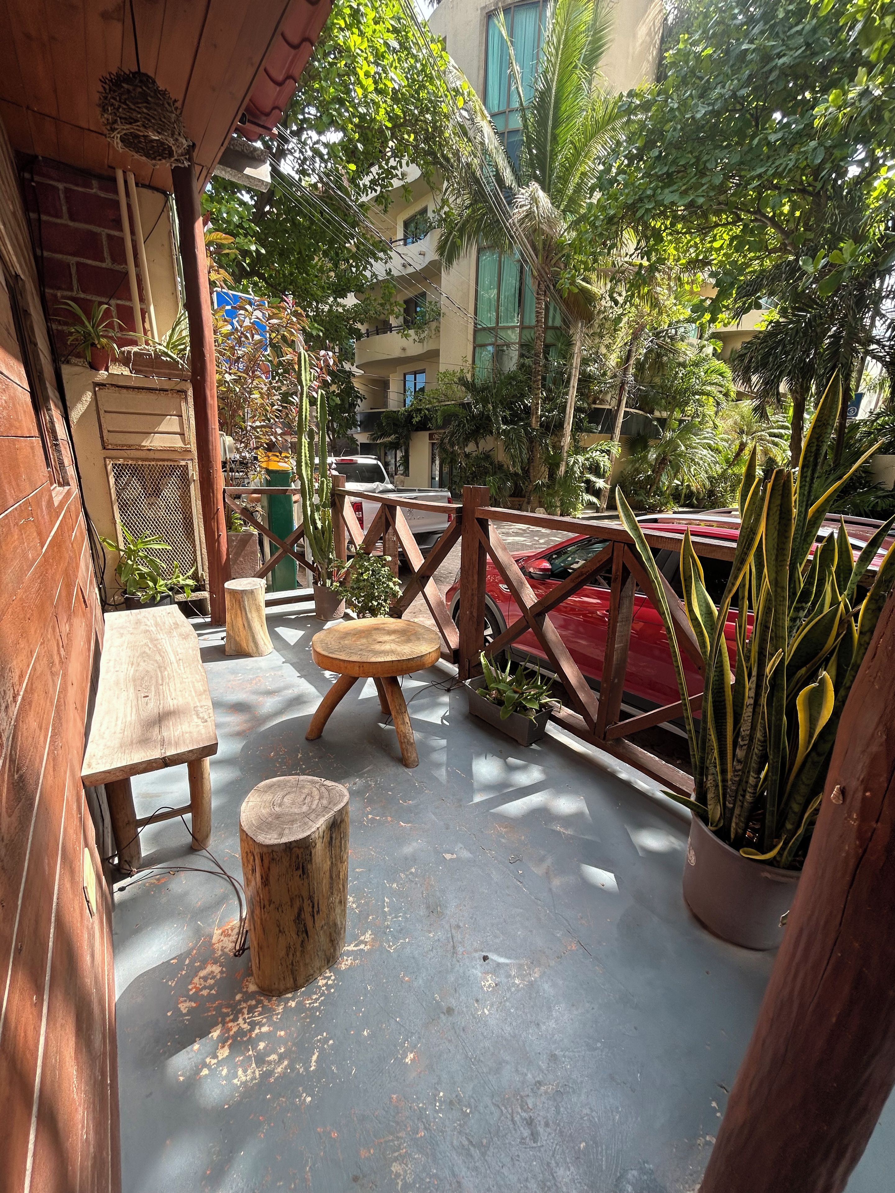 An outdoor seating area with wooden furniture, potted plants, and a view of a building in the background.