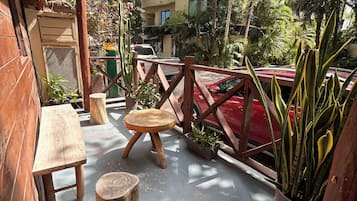An outdoor seating area with wooden furniture, potted plants, and a view of a building in the background.
