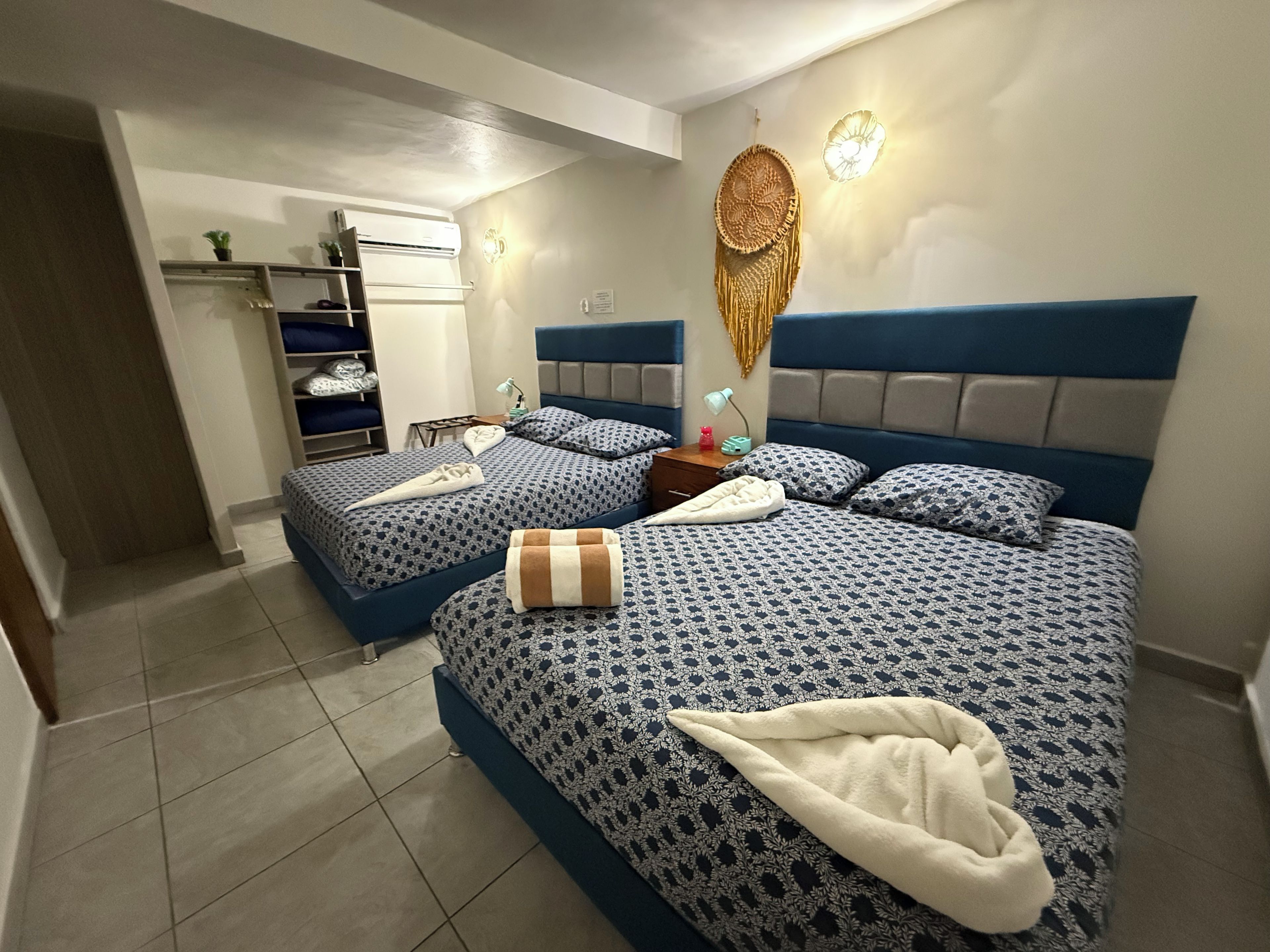 Ein Hotelzimmer mit zwei Betten, einem Schrank, einem Nachttisch und einer Wand-Klimaanlage.