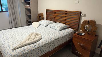 Un lit bien fait, avec une couvre-lit à motifs floraux, une tête de lit en bois et une table de chevet sur laquelle se trouvent une lampe et une télécommande.