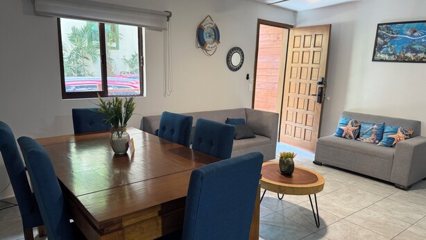 A dining area with a wooden table and blue chairs, a grey sofa, and a small round table with a plant. - Blue Angel 4, just a few steps from 5th Avenue (Playa del Carmen)