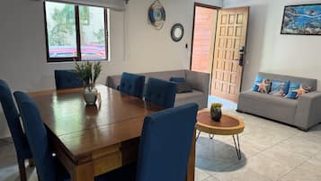 Ein Essbereich mit einem Holztisch und blauen Stühlen, einem grauen Sofa und einem kleinen runden Tisch mit einer Pflanze.