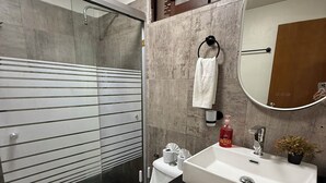 A modern bathroom with a glass shower enclosure, a toilet with a decorative seat cover, a sink with a mirror, and a small potted plant. - Blue Angel 4, just a few steps from 5th Avenue (Playa del Carmen)