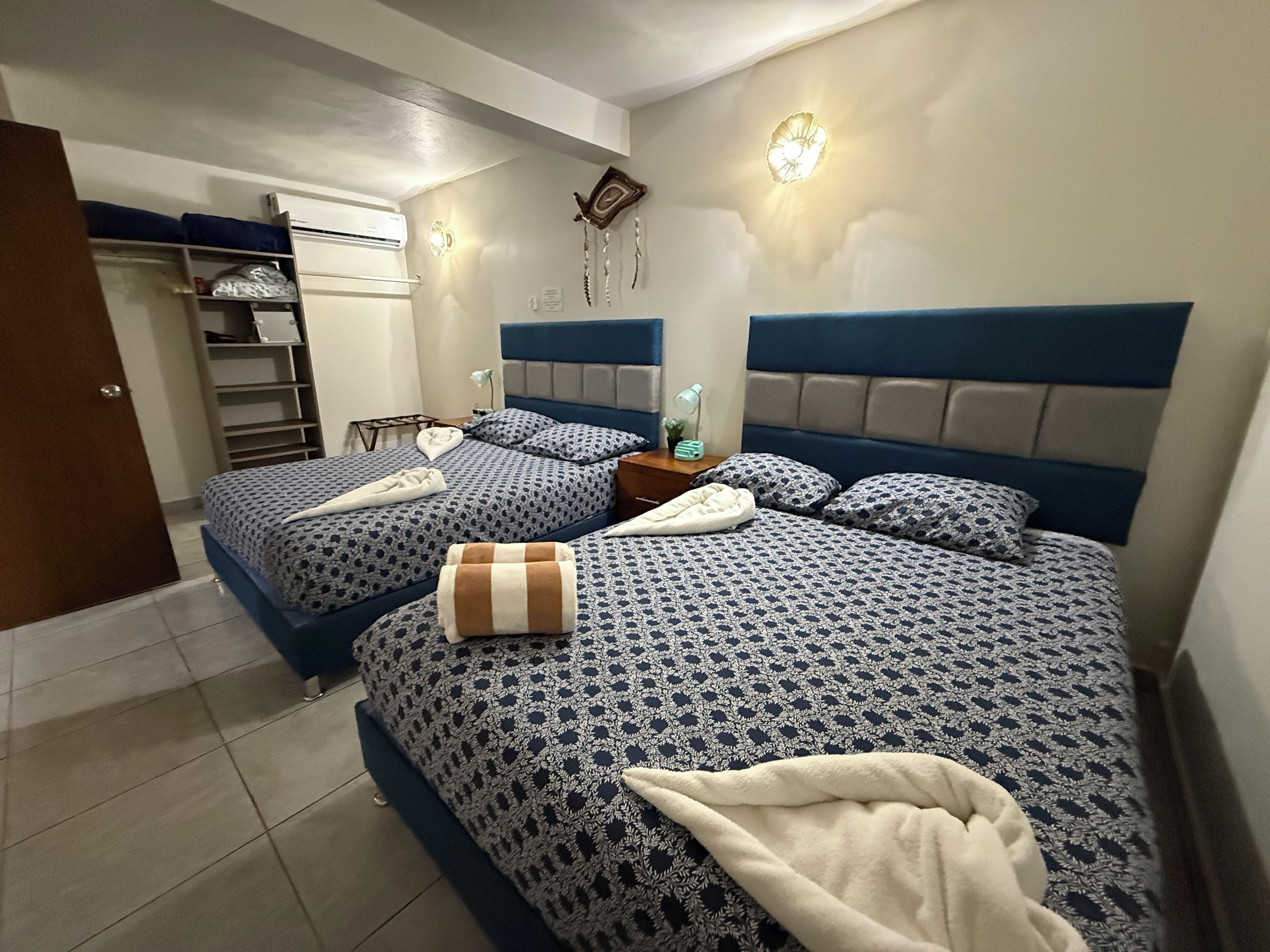A bedroom with two beds, each with patterned bedding and headboards. There is a nightstand with a lamp and a small plant on one bed.