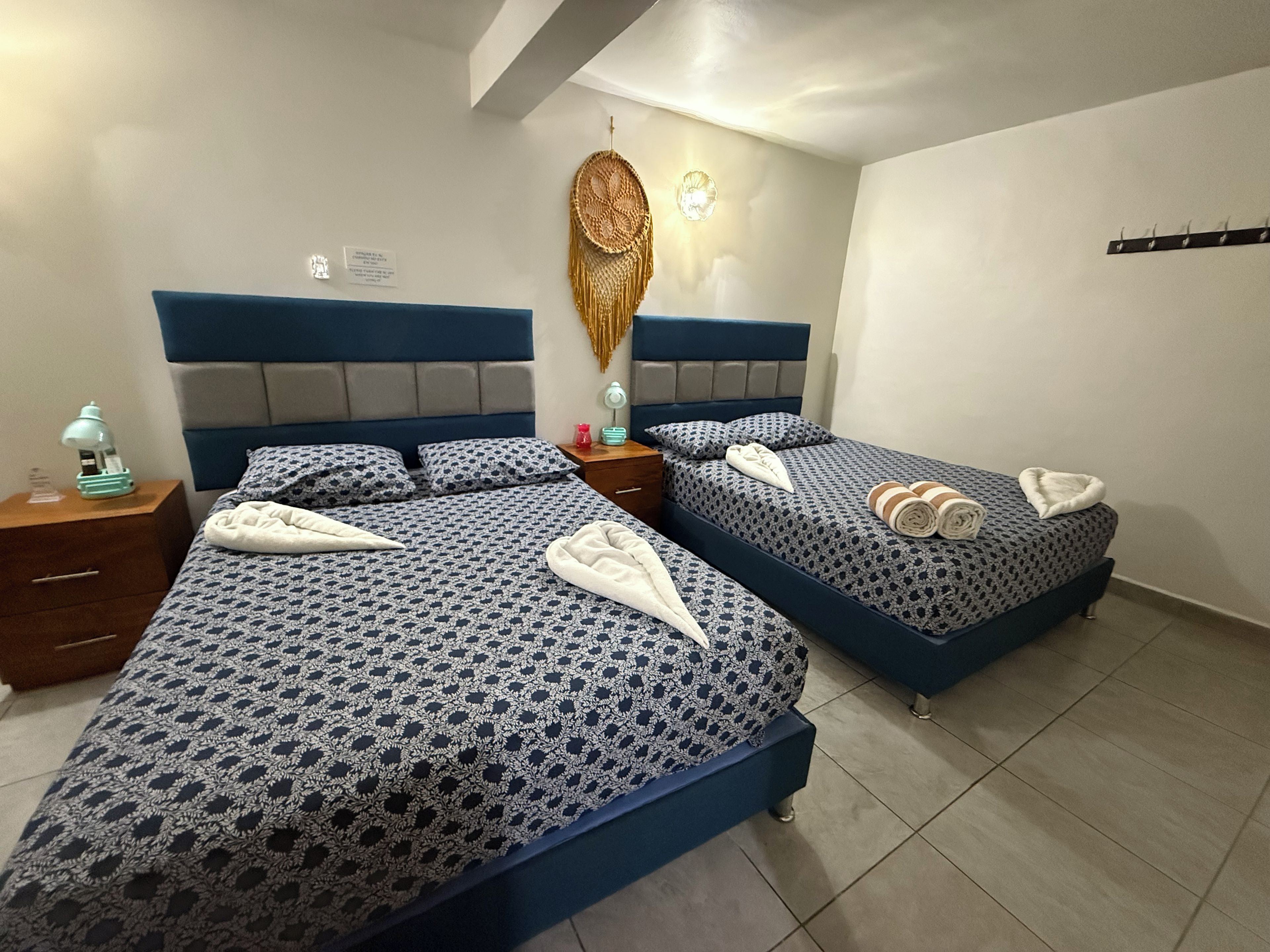 Een hotelkamer met twee bedden, elk met een geborduurde spreideken, een bedlampje en een decoratief object aan de muur.